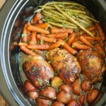 Browned honey garlic chicken thighs with potatoes, carrots, and green beans in a black slow cooker