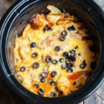 Crockpot enchilada casserole in an oval slow cooker with melted cheese, tortilla wedges, red sauce, and black olives