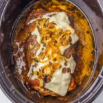 Whole Crockpot French onion meatloaf with melted Swiss and browned onions in an oval cooker