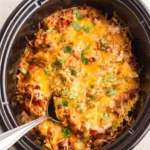 Crock Pot Mexican lasagna with melted cheese and cilantro, scooped from a black oval slow cooker