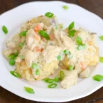 Crock Pot chicken pot pie filling over split golden biscuits on a white plate with sliced green onions