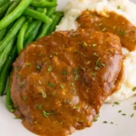 Crockpot cube steak and gravy with parsley, mashed potatoes, and green beans on a dinner plate