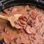 Crock Pot Cajun red beans and andouille in creamy sauce, with a wooden spoon inside the slow cooker