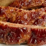 Overlapping bone-in Crockpot BBQ ribs coated in glossy reddish-brown sauce on a light plate