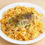 No peek chicken casserole with a whole seasoned breast over creamy golden rice and parsley