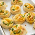 Broccoli cheese pinwheels with golden dough spirals on a parchment-lined baking sheet