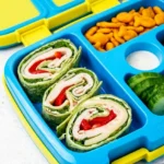 Three turkey and cheese pinwheels with green and red layers in a blue divided lunchbox