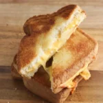 Air fryer grilled cheese cut into two stacked triangles with golden toast and melted cheese on a wooden board