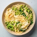 Parmesan pea spaghetti with whole green peas and wilted spinach in a shallow beige bowl