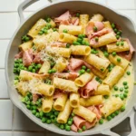 Family-style pan of rigatoni with folded pink ham, green peas, and grated Parmesan