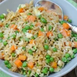 Bowl of chicken fried rice with separate rice grains, peas, diced carrots, chicken, and egg