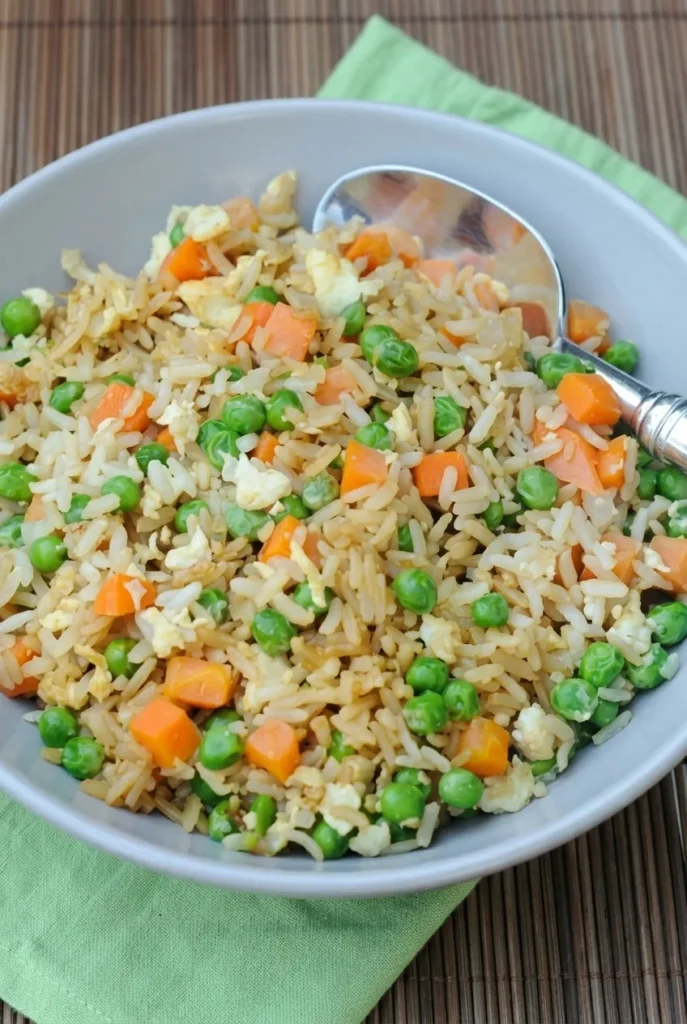 Bowl of chicken fried rice with separate rice grains, peas, diced carrots, chicken, and egg