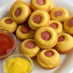 Mini corn dog muffins with visible hot-dog centers on a white platter beside ketchup and mustard.