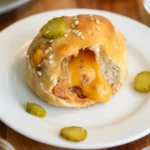 Opened sesame-topped cheeseburger biscuit bomb with beef, melted orange cheese and a pickle slice