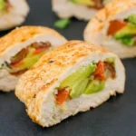 Thick-cut chicken avocado roll-ups with golden chicken exteriors and visible tomato filling on a dark platter