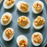 Classic deviled eggs with spooned yellow filling and paprika on a dark blue-gray platter
