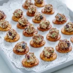 Mini cranberry pecan cheese balls, each on a round cracker, arranged on a pale serving tray