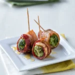 Three whole bacon-wrapped Brussels sprouts with upright picks and a light maple drizzle on a white square plate.