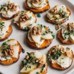 Sweet potato crostini topped with goat cheese, thin pear slices, walnuts, and greens on a light platter
