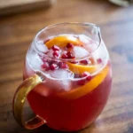 Pomegranate Thanksgiving punch over ice in a clear glass with orange slices and pomegranate arils