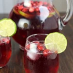 Cranberry ginger ale punch with ice, whole cranberries and a lime wheel, served beside a glass pitcher
