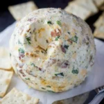 Uncoated bacon ranch cheese ball with a scoop removed, served on parchment with crackers
