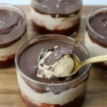 Clear chocolate peanut butter yogurt cups with three layers and a spoon breaking into the front cup