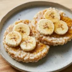 Two peanut butter and banana rice cakes with honey and cinnamon on a pale gray plate