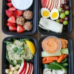 Four different healthy snack boxes with fruit, yogurt, egg, tuna-avocado salad, and hummus with vegetables