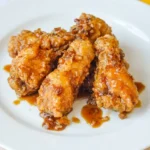 Honey garlic chicken wings piled on a white plate, with craggy golden coating and glossy garlic-speckled glaze.