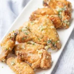 Garlic Parmesan chicken wings on a white platter, with golden skin, pale cheese and garlic, and parsley
