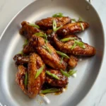 BBQ chicken wing flats and drumettes with glossy glaze and green onions in an oval metal pan