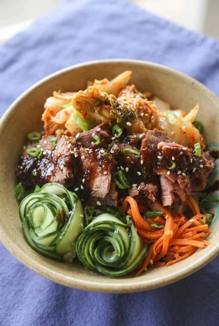 Korean BBQ steak rice bowl with glossy beef, kimchi, cucumber ribbon coils, julienned carrots, scallions, and sesame