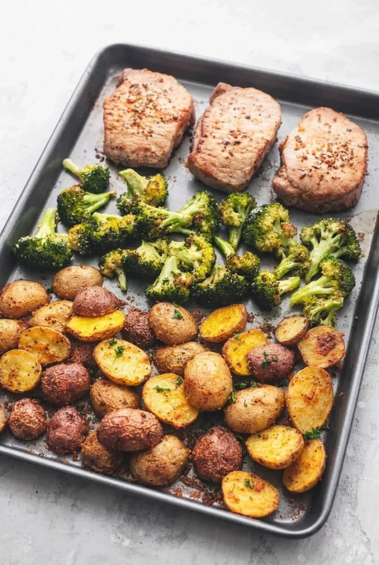 Sheet Pan Pork Chops with Potatoes and Broccoli, arranged in separate zones on a dark pan