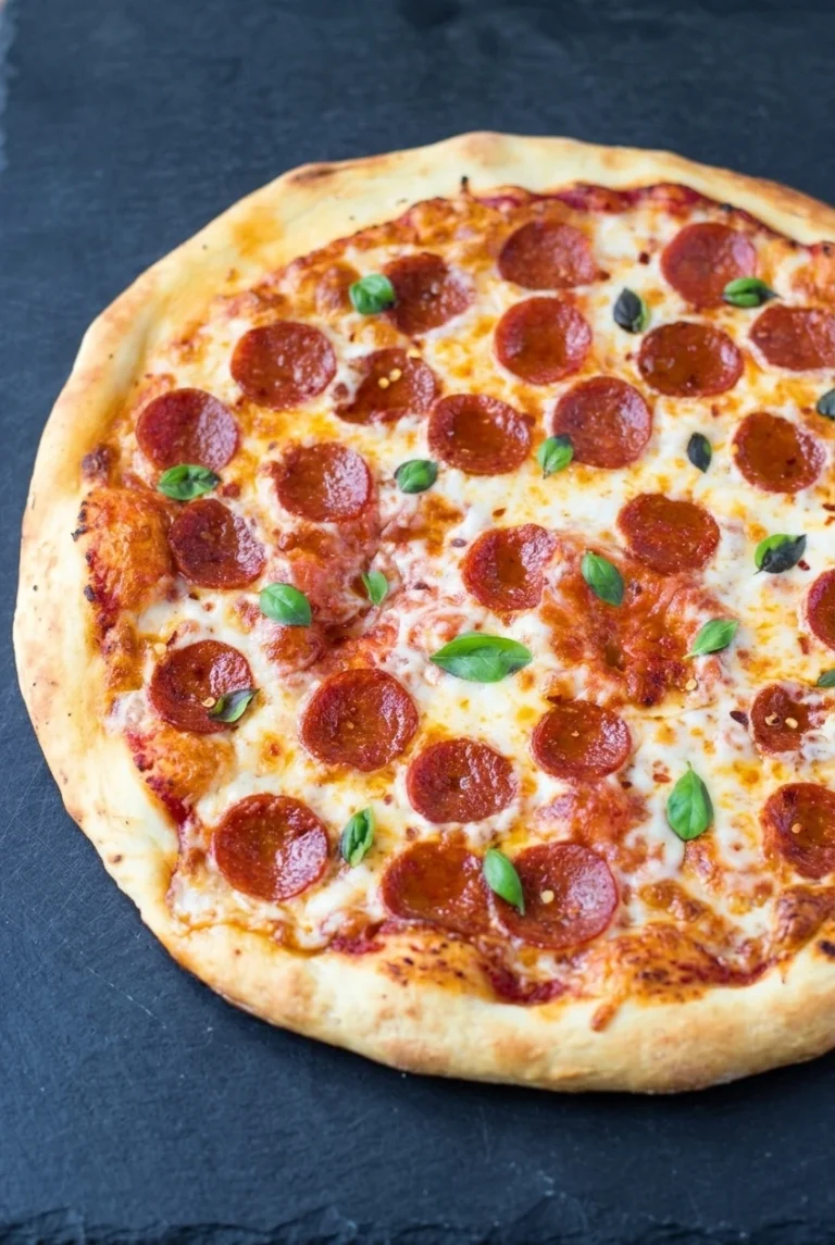 Classic Pepperoni Pizza with a Puffy Golden Crust Whole uncut classic pepperoni pizza with a puffy golden crust, melted mozzarella, and fresh basil on dark slate.