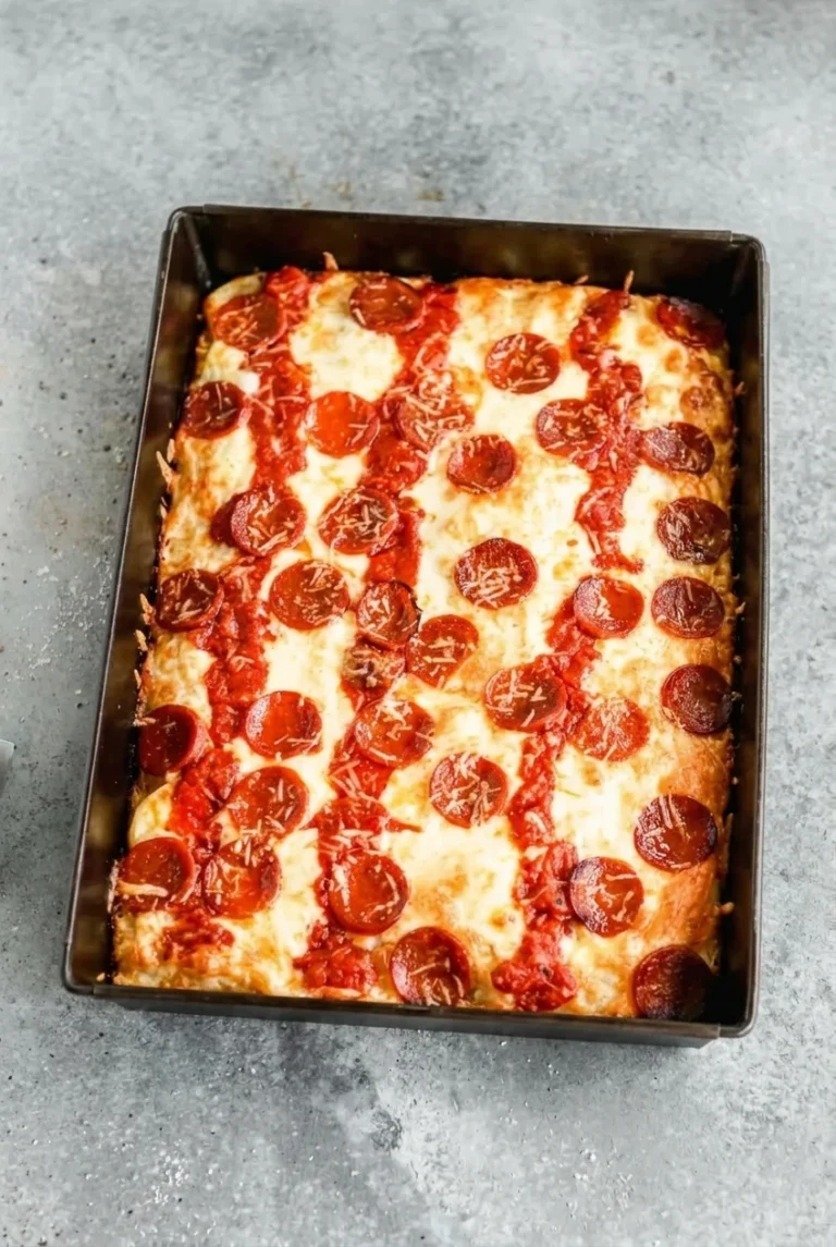Whole pepperoni Detroit-style pan pizza with striped sauce and browned cheese edges in a dark rectangular pan