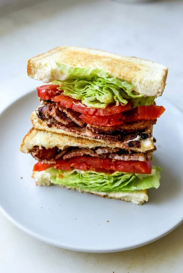 Classic BLT sandwich cut into two stacked halves, showing crisp bacon, ripe tomato, iceberg lettuce, and white toast.