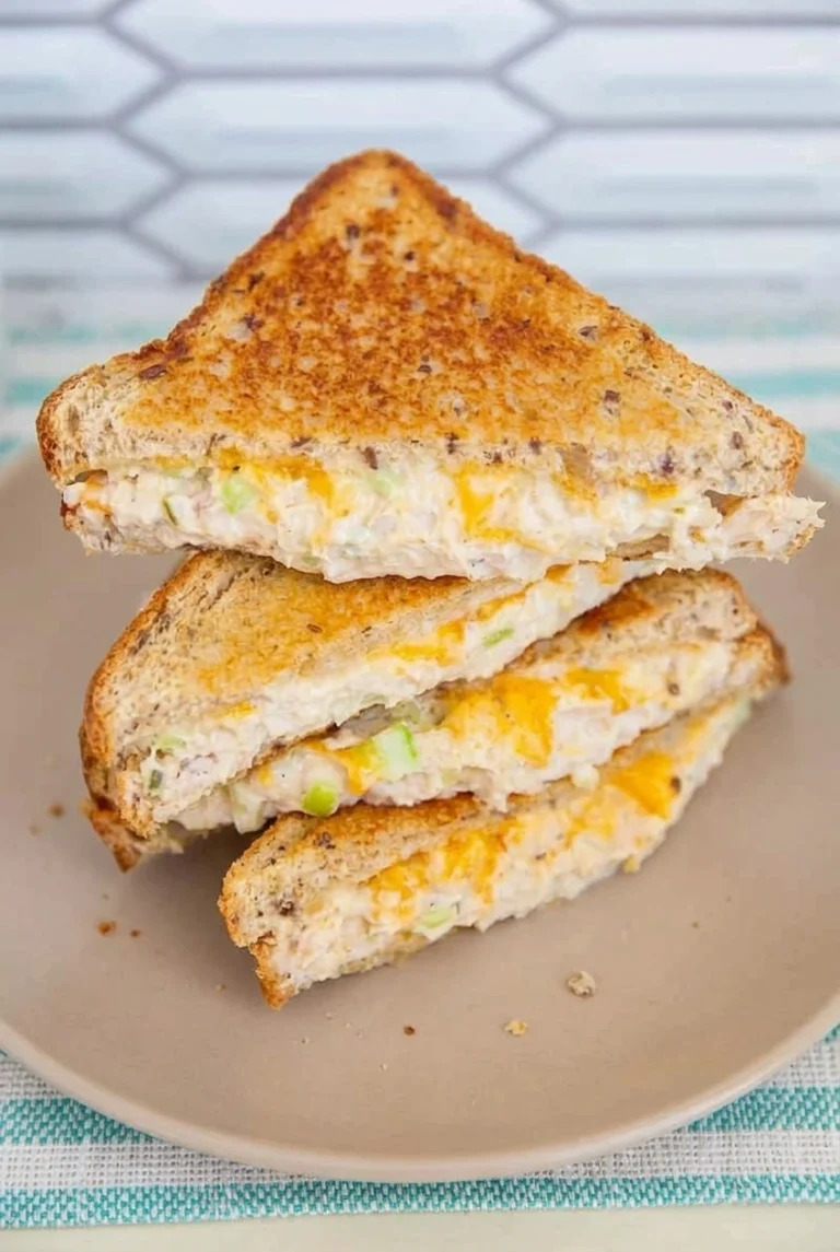 Golden multigrain tuna melt halves stacked on a plate, with creamy celery tuna and melted cheddar visible.