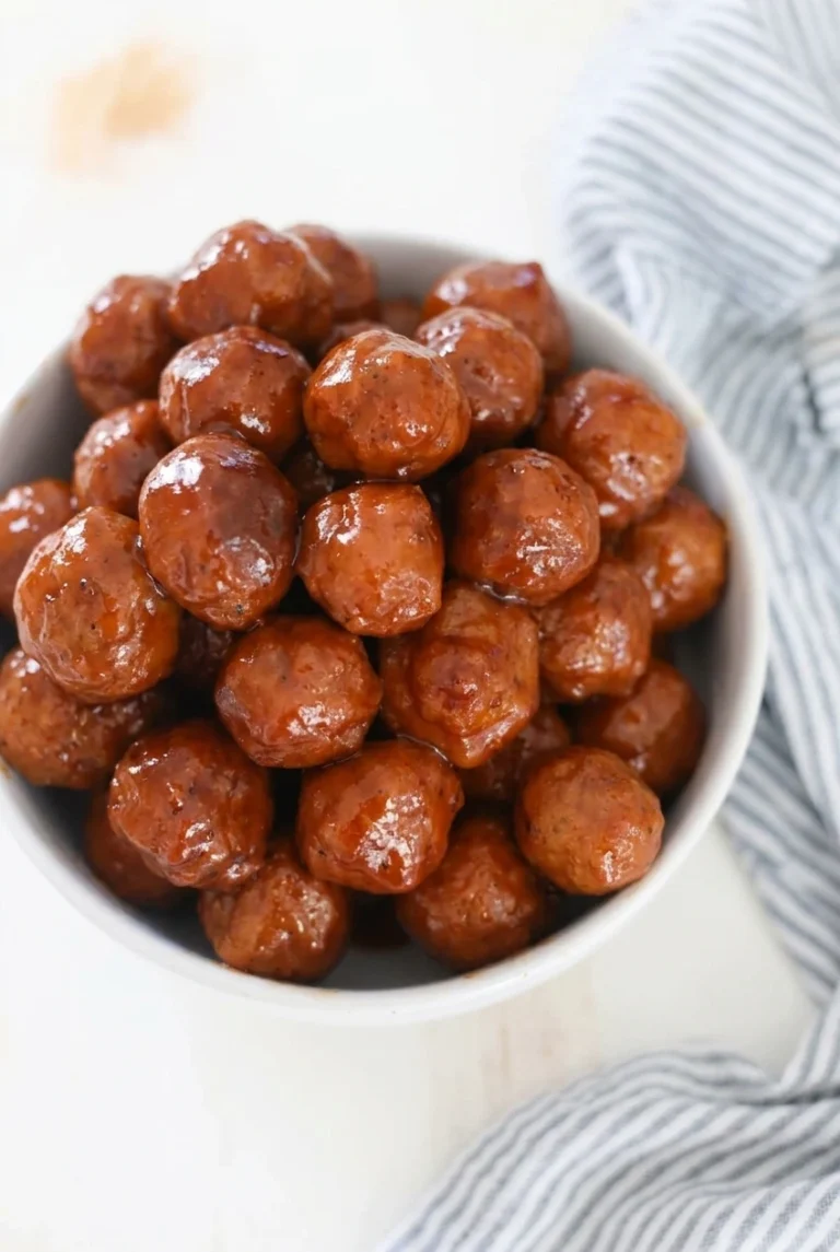 Slow Cooker BBQ Meatballs with Grape Jelly Slow Cooker BBQ Meatballs piled in a white bowl, coated in glossy reddish-brown sauce