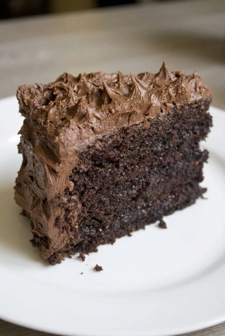 A thick wedge of moist chocolate birthday cake with two dark layers and rustic chocolate buttercream on a white plate.