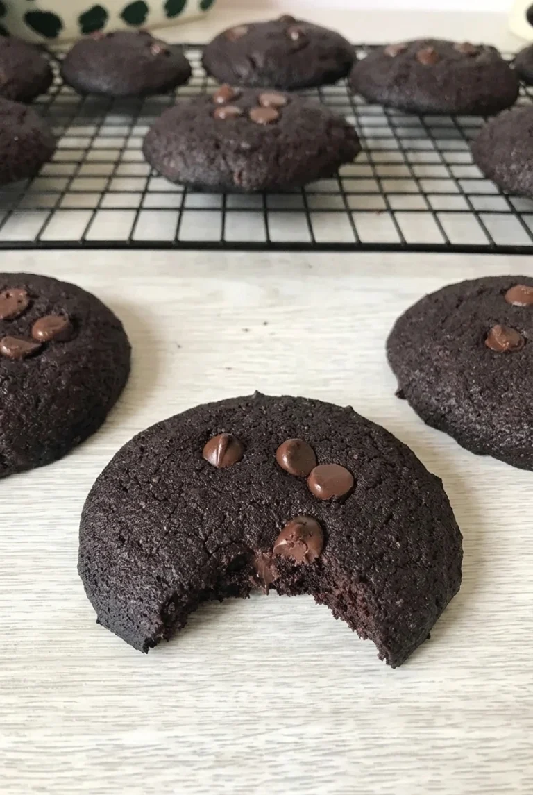 Sugar-Free Chocolate Chip Cookies with Dark Cocoa Dark cocoa sugar-free chocolate chip cookies, with a soft-centered bitten cookie in front and whole cookies behind