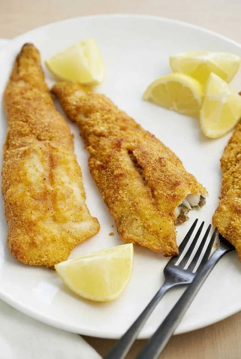 Golden air fryer fish fillets with lemon wedges and lemon garlic butter on a white plate.