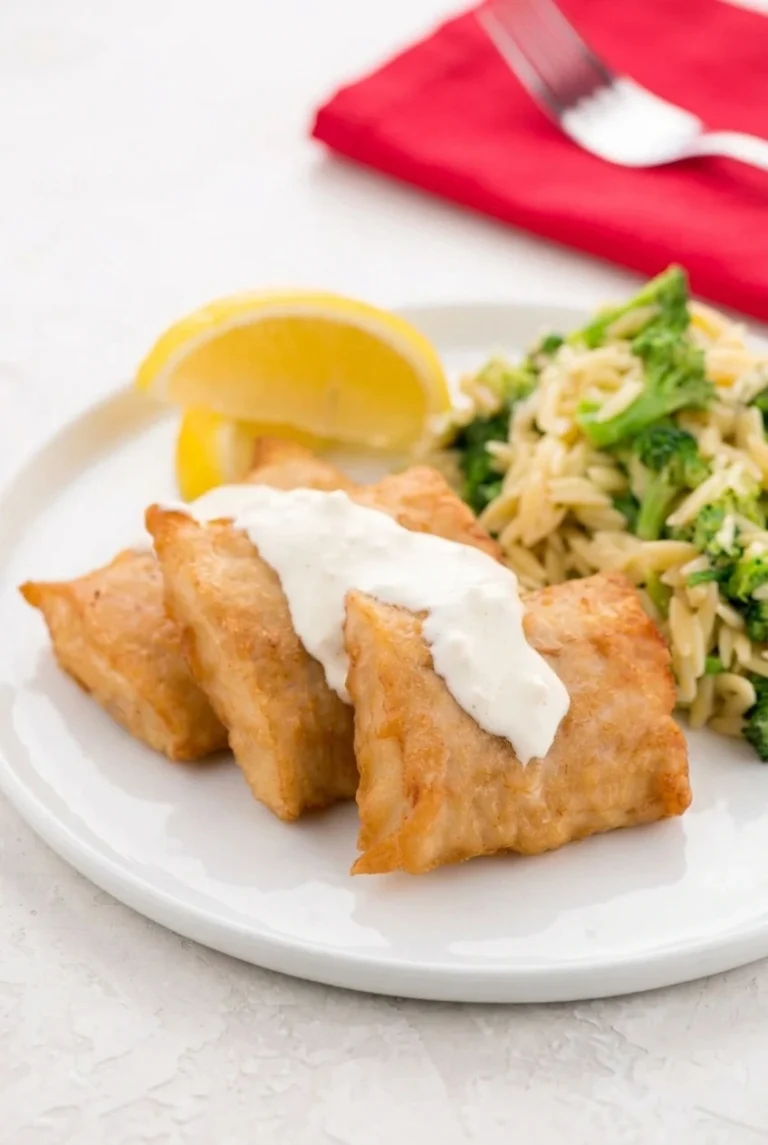 Golden crispy fish bites with garlic aioli drizzle and green herbs on a white plate