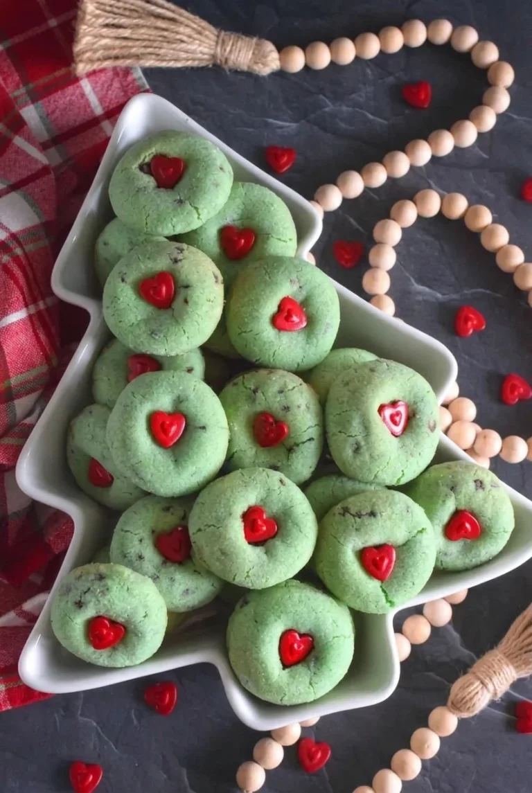 Grinch cookies with red heart sprinkles arranged on a white tree-shaped platter