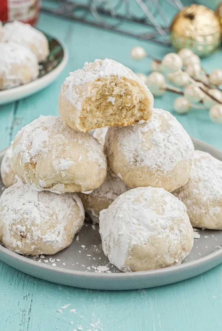 Classic Pecan Snowball Cookies Pecan snowball cookies piled on a pale ceramic plate, with a broken cookie showing its pecan-speckled crumb