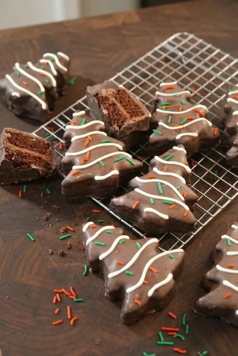 Homemade Chocolate Christmas Tree Cakes Chocolate Christmas Tree Cakes with white drizzle and holiday sprinkles, including one cut open to show the filling.