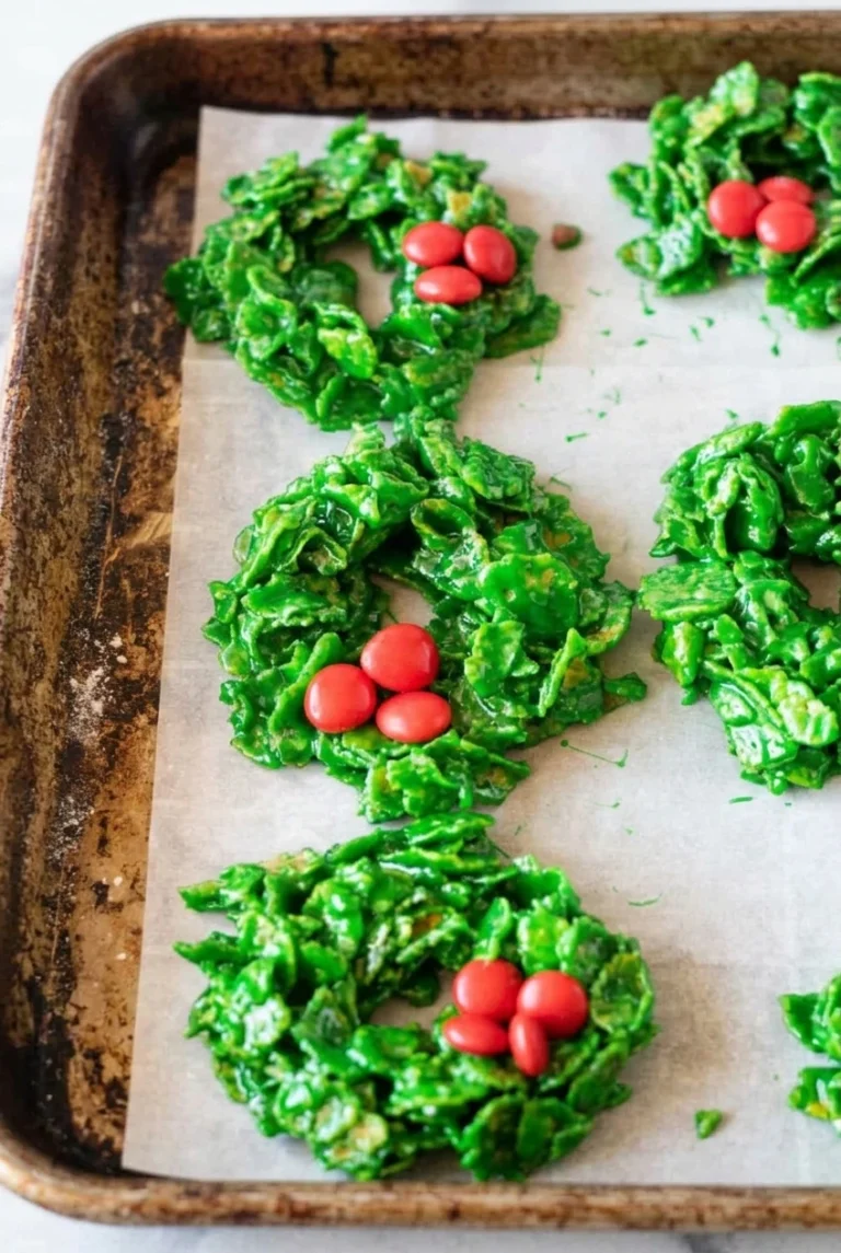 Christmas Cornflake Wreath Cookies (No-Bake) Rustic green Christmas Cornflake Wreath Cookies with visible cornflakes and red candy clusters on parchment