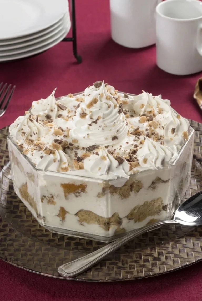 Christmas tiramisu trifle with visible pound cake and mascarpone layers, piped cream, and chopped toffee in a clear bowl