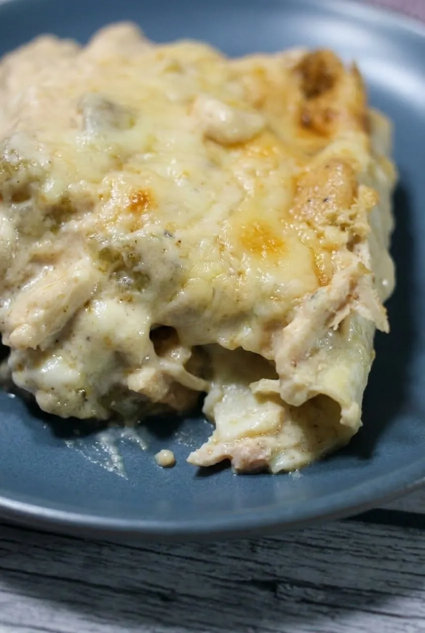 Close view of creamy sauce, melted cheese and shredded chicken at the edge of a white chicken enchilada