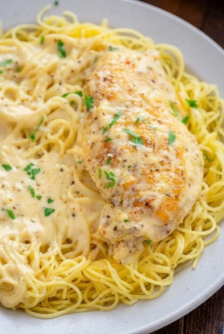 Close view of lightly golden chicken, creamy sauce, and distinct angel hair strands